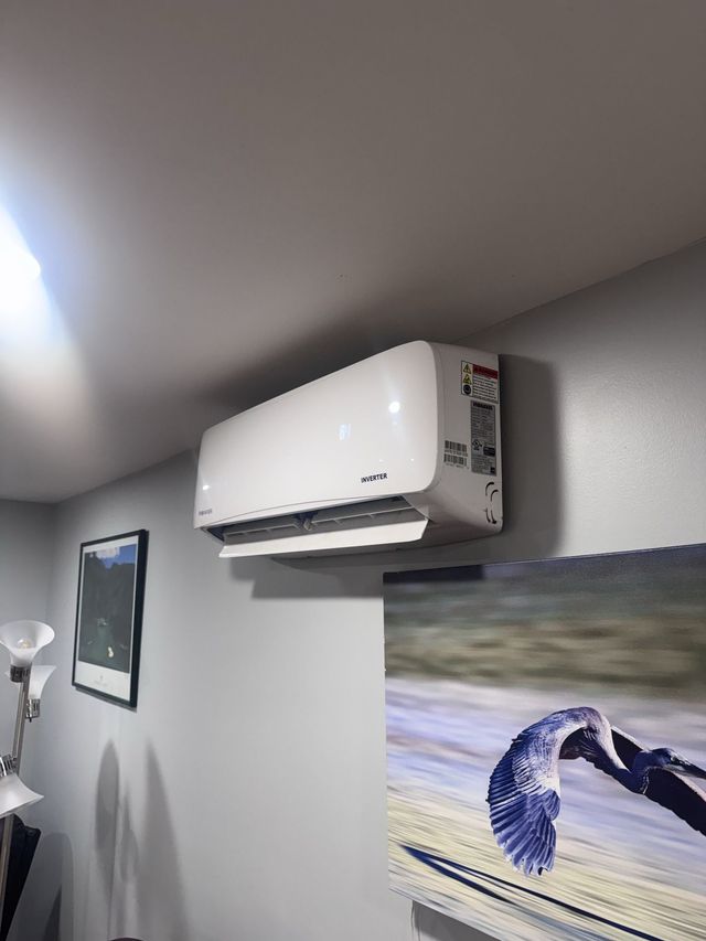 Wall-mounted white air conditioner above a blue bird wall print in a gray room