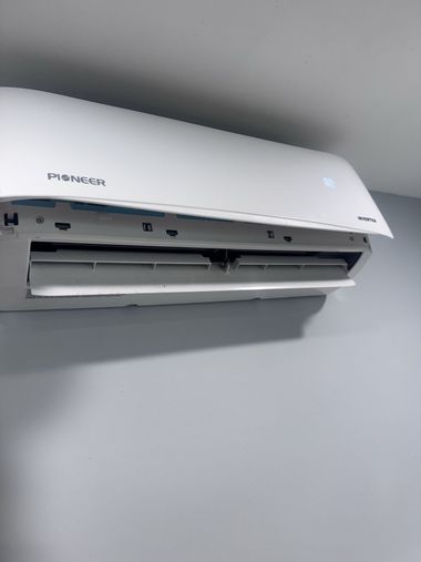White wall-mounted air conditioner with front panel open against a gray wall.