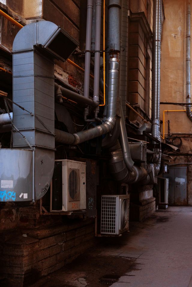 Narrow alley with industrial pipes, vents, and brick walls in dim light