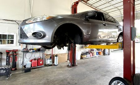 A grey sedan raised on a yellow hydraulic automotive lift inside a repair shop.