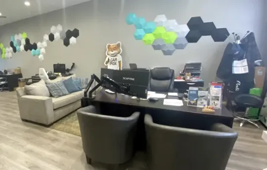 Office interior with a desk, chairs, a sofa, and hexagonal wall art featuring light blue, green, and dark gray tiles.