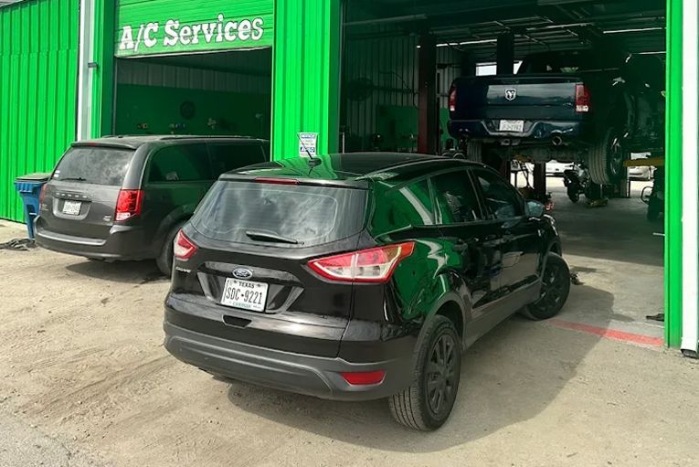 Two parked cars outside a green auto service garage with a vehicle lift inside