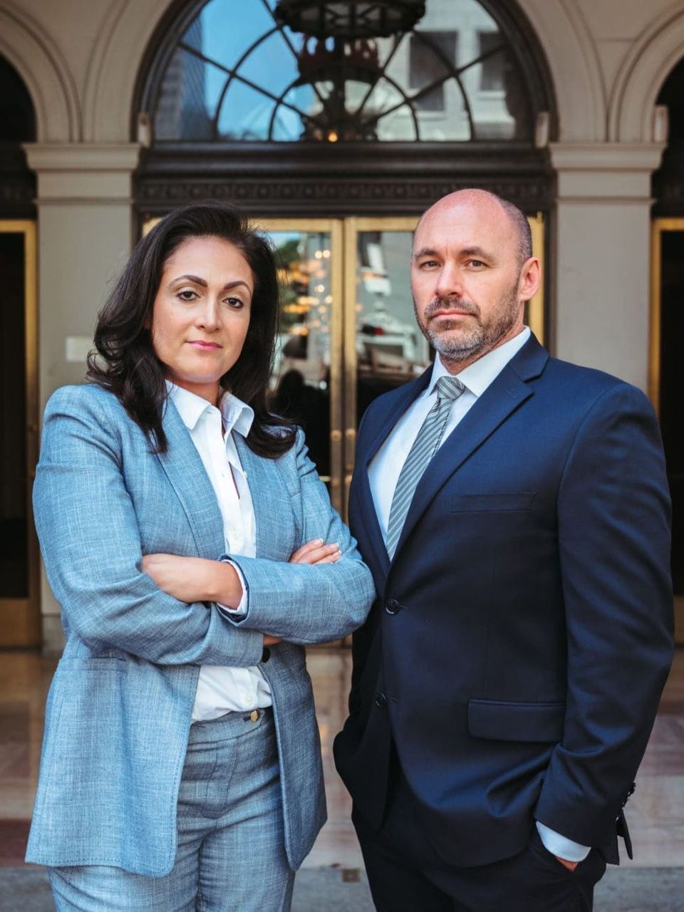 A man and a woman in suits are standing next to each other in front of a building.