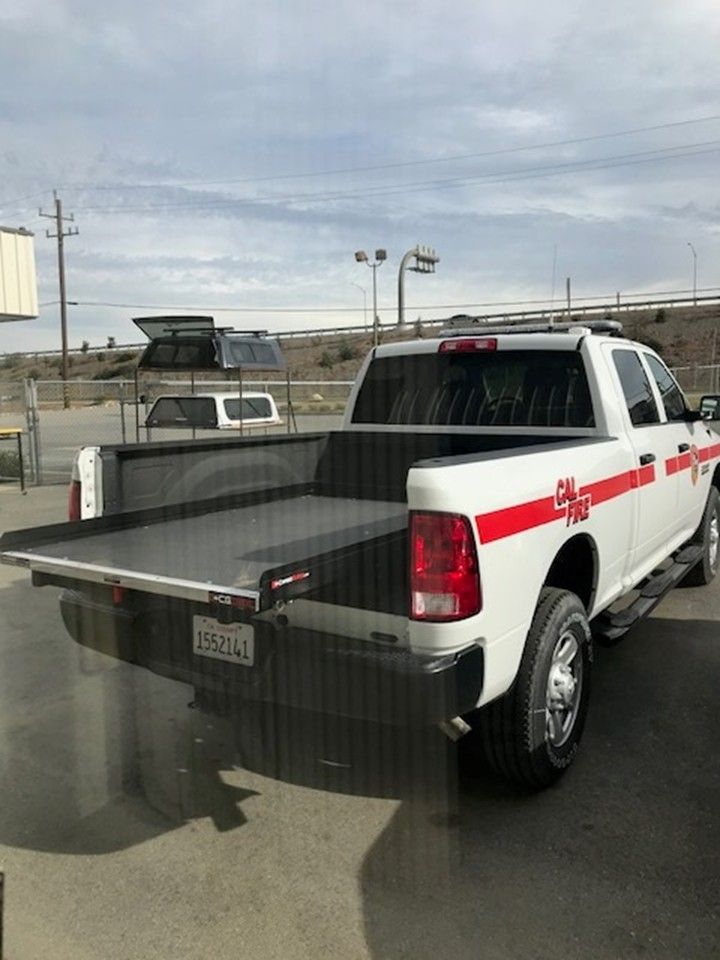 A white pickup truck with a red stripe and an extended cargo slide in the open truck bed, parked in an outdoor lot.