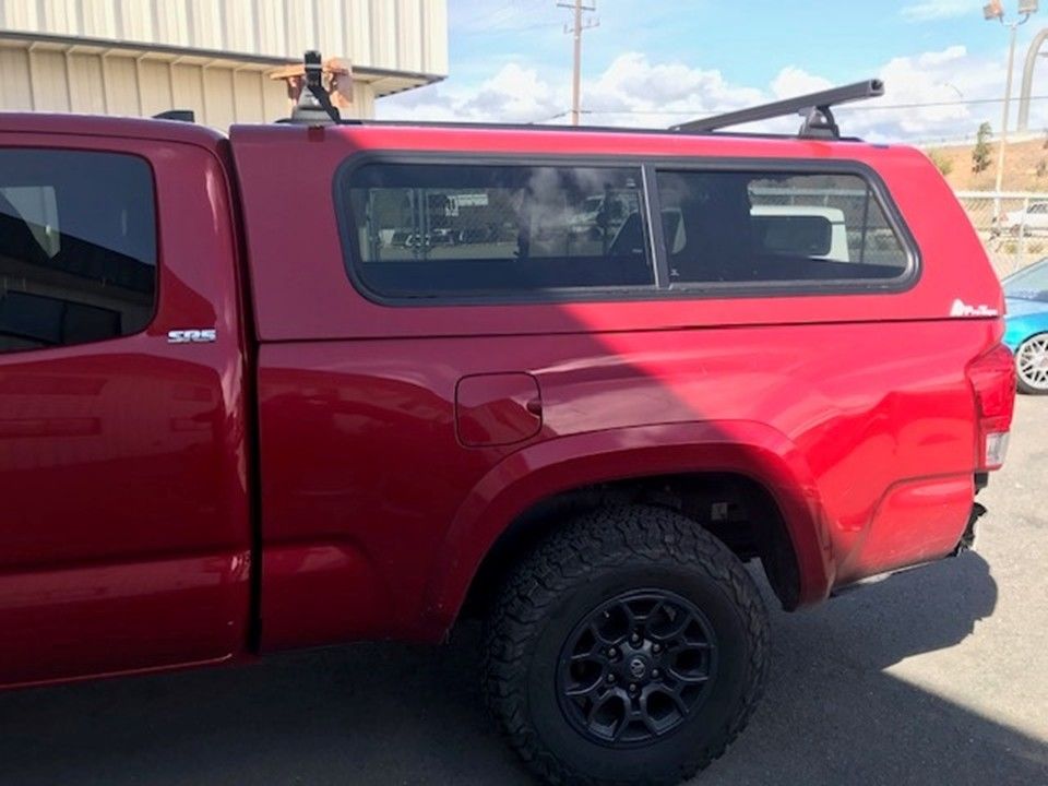 A side view of a red pickup truck with a matching bed cap and a roof rack parked on an asphalt lot.
