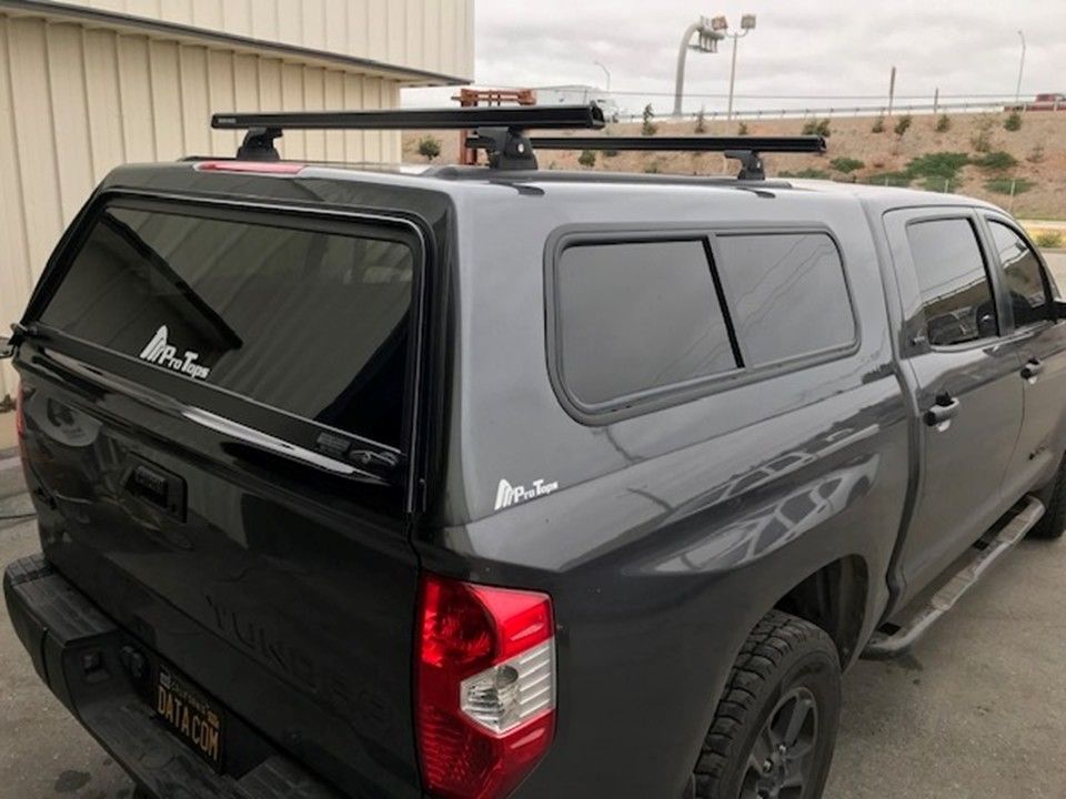 A grey pickup truck featuring a color-matched camper shell with a black roof rack mounted on top.