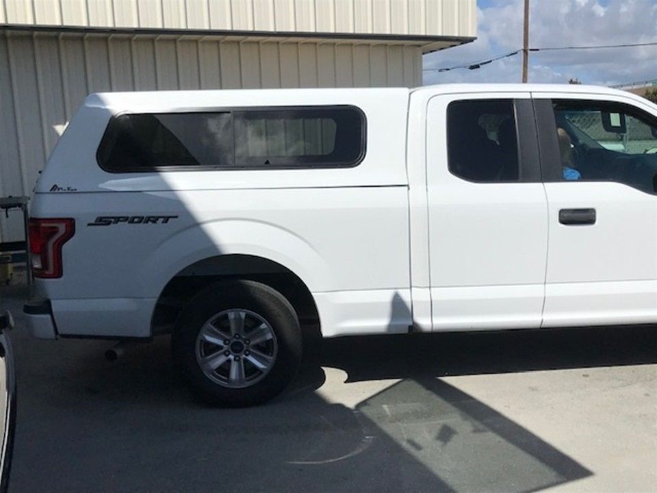 A white Ford F-150 Sport pickup truck with a matching white camper shell parked on a concrete surface.