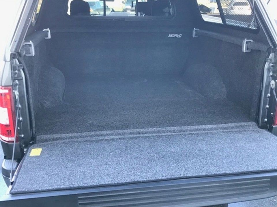 An open pickup truck bed with a gray carpeted liner and a matching tailgate cover, viewed from the rear.