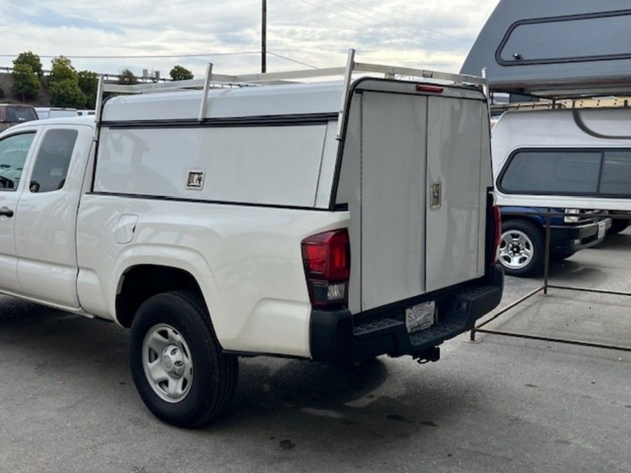 White pickup truck parked outdoors, featuring a white camper shell and a metal rack on top.