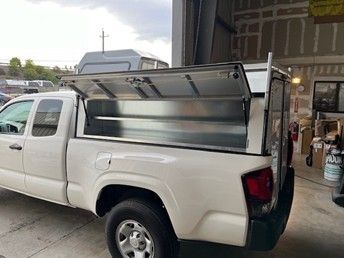 White pickup truck parked inside a garage with a custom metal utility storage box open on its bed.