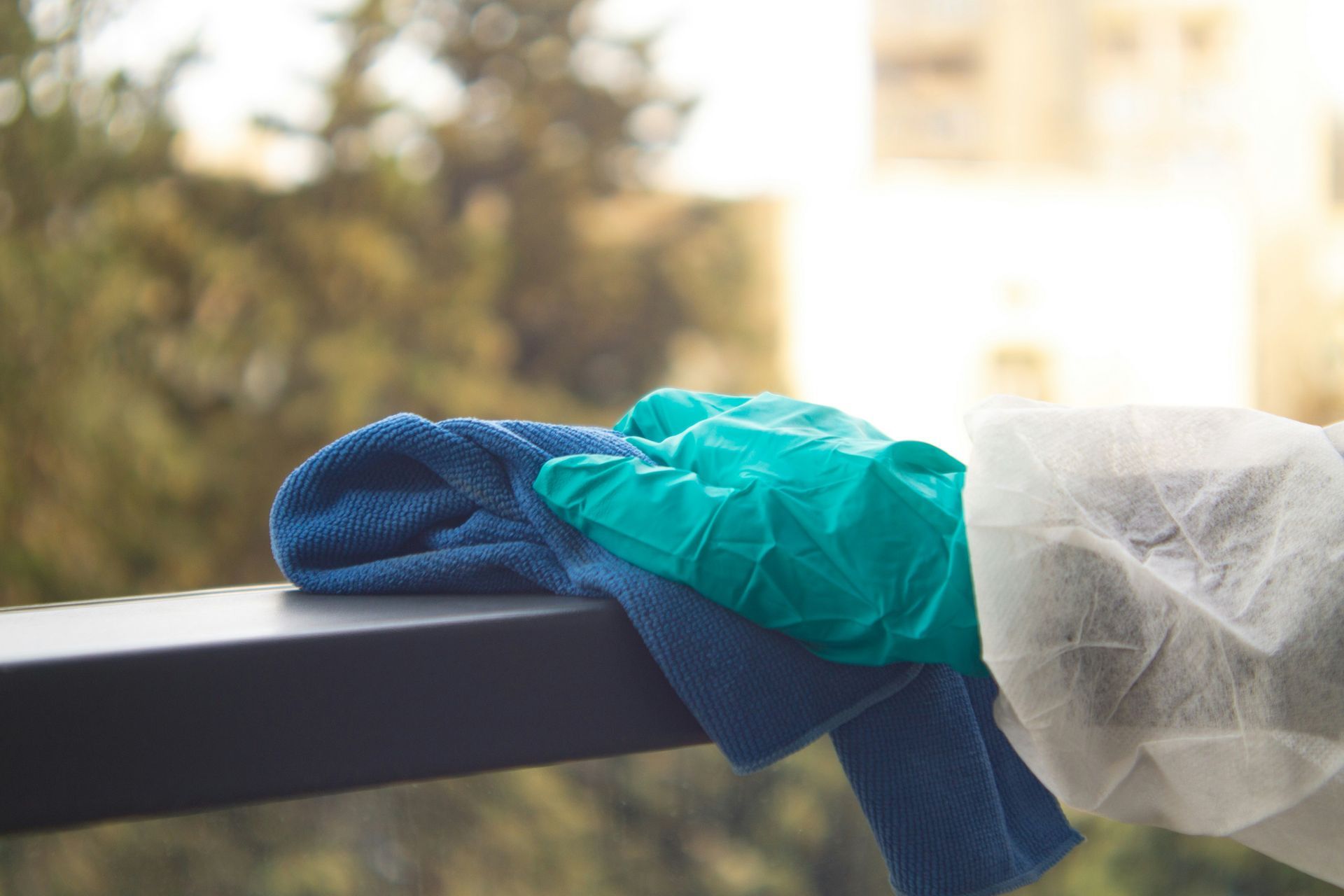 Blue cloth, green glove, and white cover on a railing against a blurred outdoor background.
