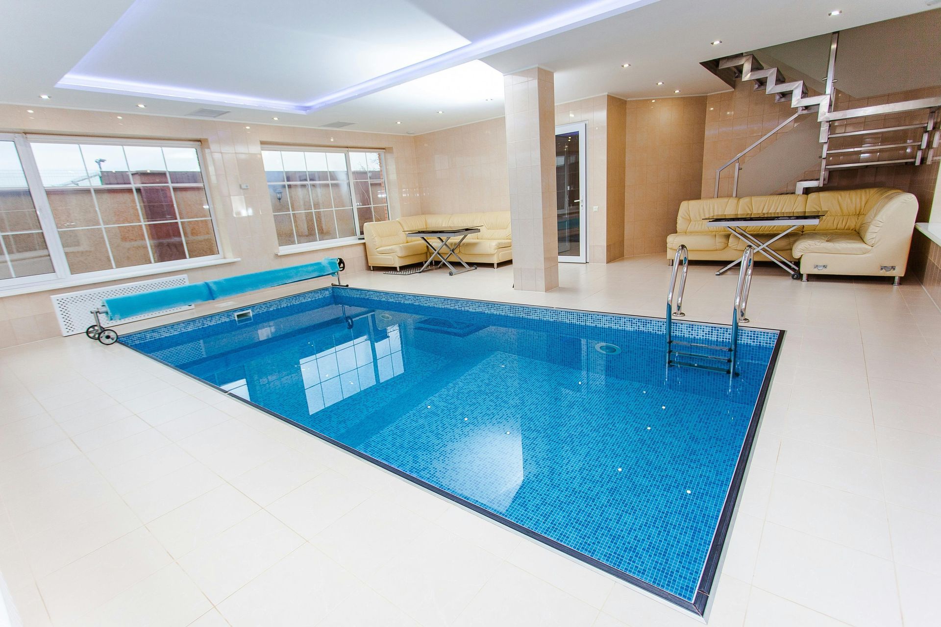 Indoor swimming pool with blue tile surrounded by cream-colored walls, floor, and sofas.