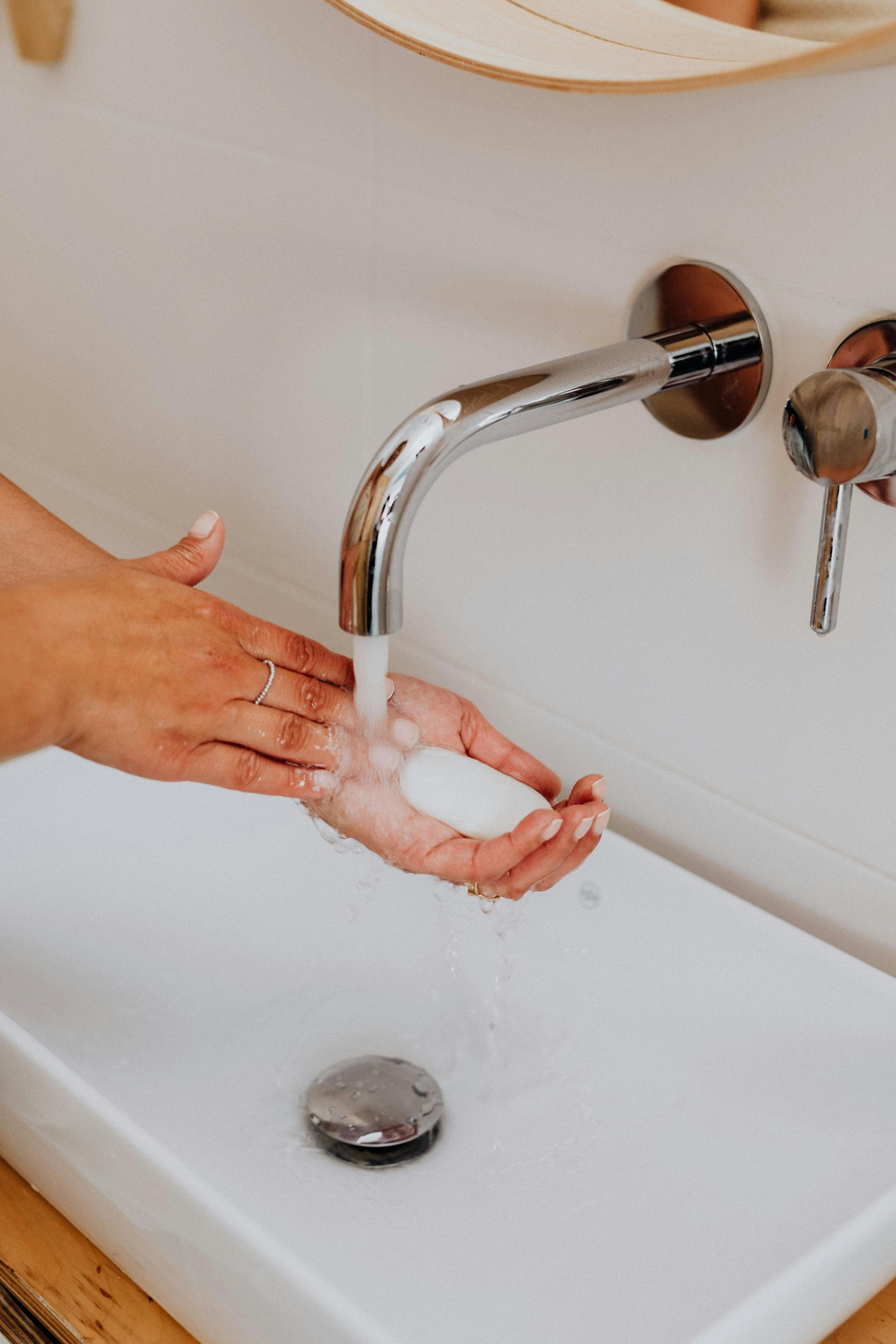 Person washing hands with soap under a faucet in a white sink.