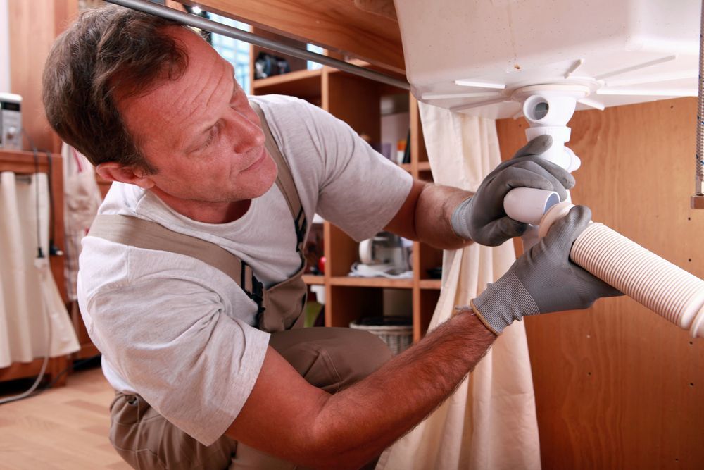 A Worker in Tan Work Boots Reaches Into a Narrow Utility Closet — Kingdom Plumbing Services in Gordonvale, QLD