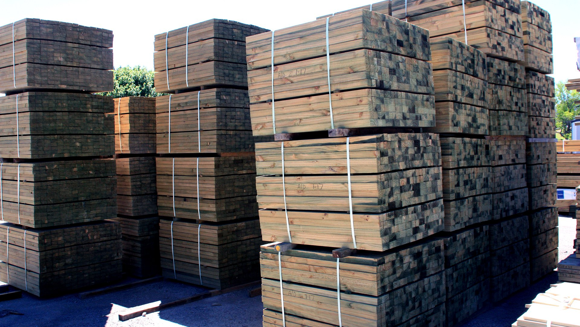Multiple stacks of bundled, dark-toned wooden planks stored outdoors on a concrete surface.