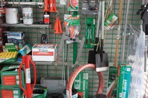 A retail display of farm and fencing tools, including shovels, wire tensioners, and various hardware in boxes.