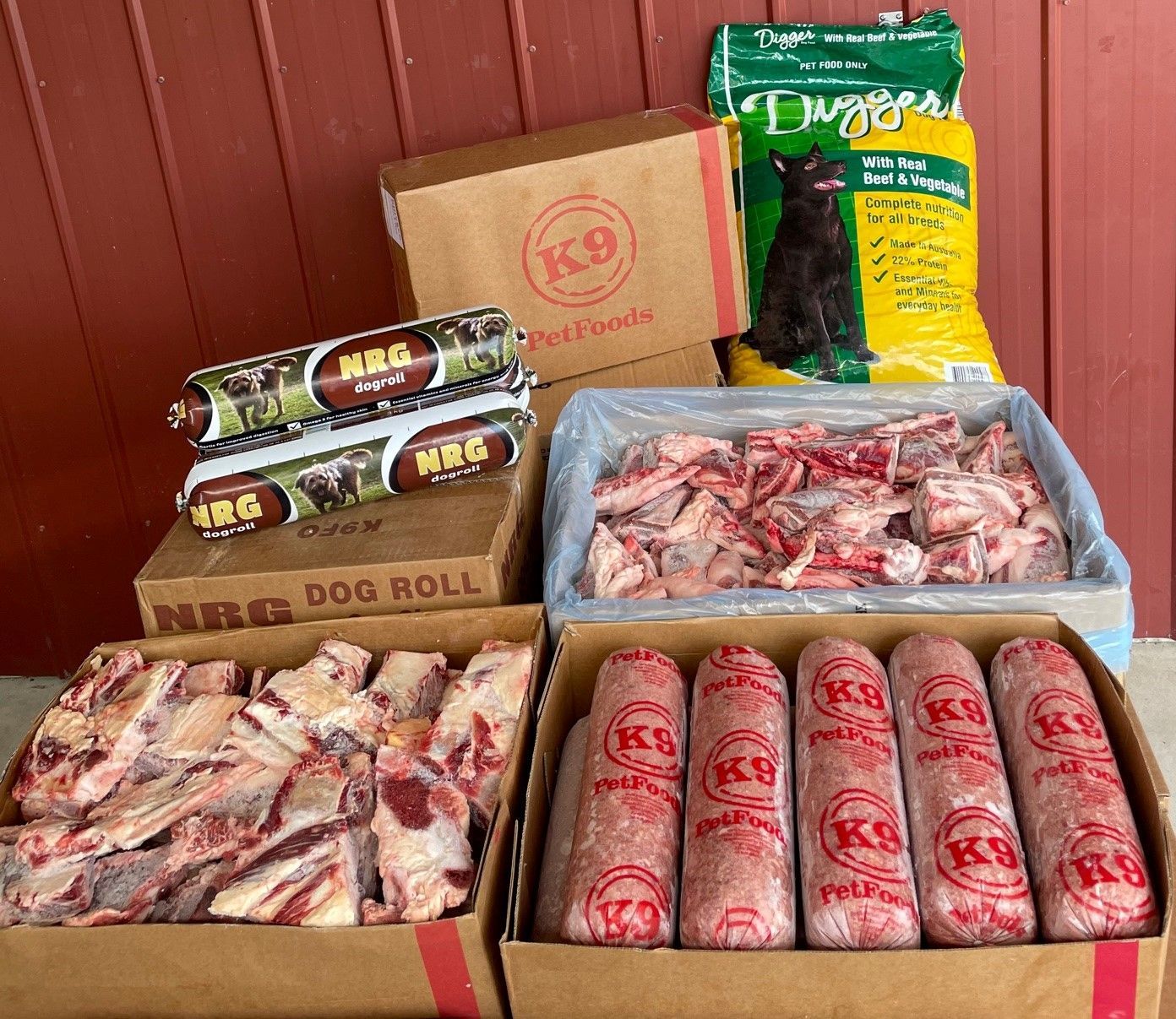 A collection of raw dog food supplies, including cardboard boxes, frozen meat rolls, and packages of raw meat bones.