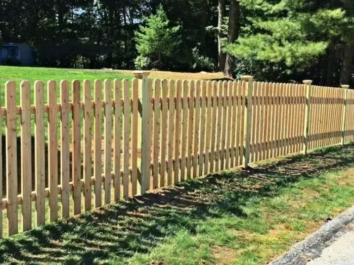 Wooden picket fence along a grassy yard, under a sunny sky.