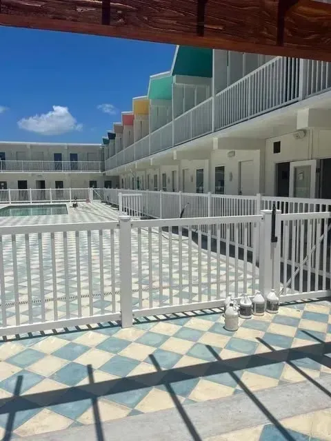 White motel with colorful rooftop accents, pool and checkered floor, sunny outdoor setting.