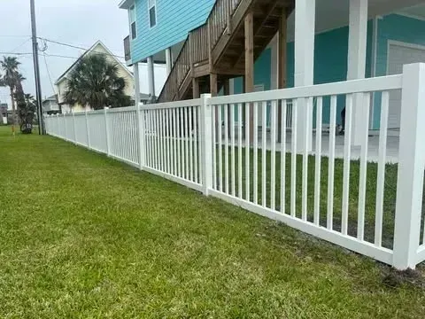 White picket fence along a grassy yard, beside a turquoise house and stairs.