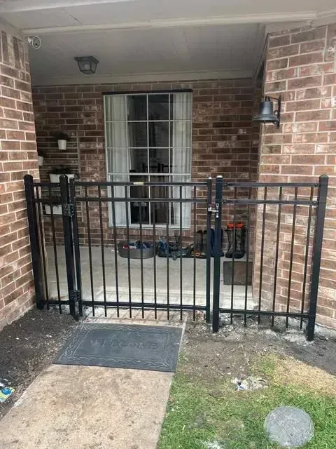 Black metal gate encloses a small porch with brick walls. A bell hangs on the right wall.