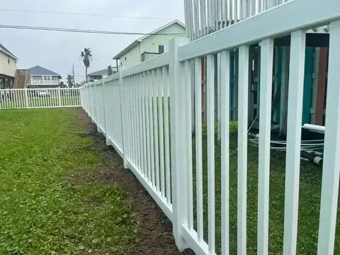 White picket fence lines a grassy yard, houses in background.