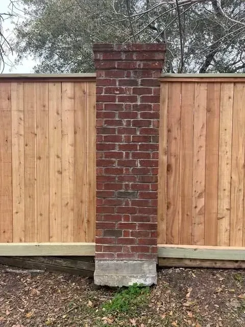 Red brick pillar against a wooden fence. Ground level view.