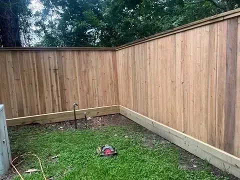 Wooden fence in a grassy yard, a circular saw on the ground.