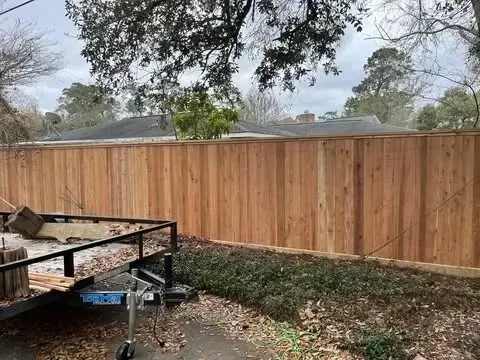 Wooden fence in a backyard, with a trailer in front. Overcast sky.