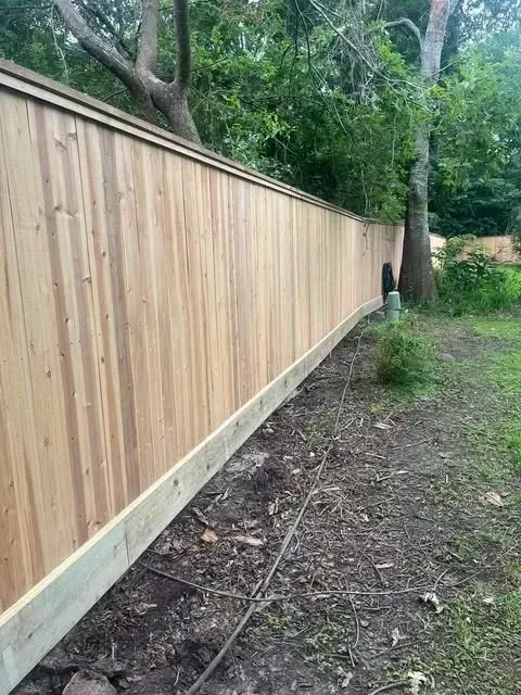 Wooden privacy fence with a curved bottom edge, in a yard with trees.