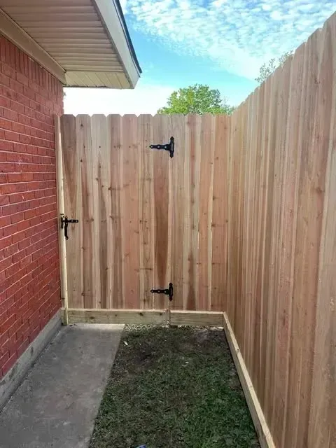 Wooden gate and fence next to a brick wall. Bright sky in background.