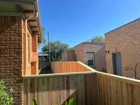 Wooden fence in a yard between two brick buildings under a clear, blue sky.