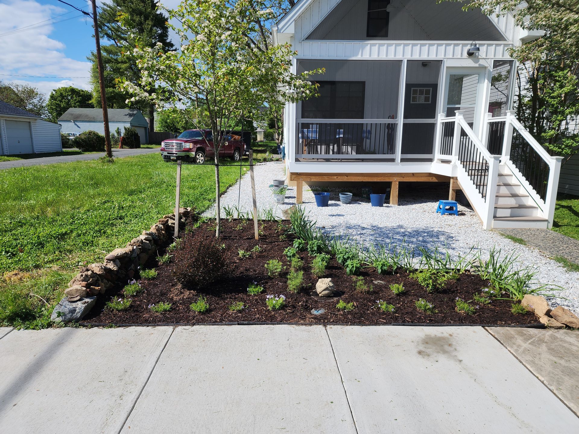 Small house with porch and front yard garden. Dark mulch, light gravel pathway, and green grass.