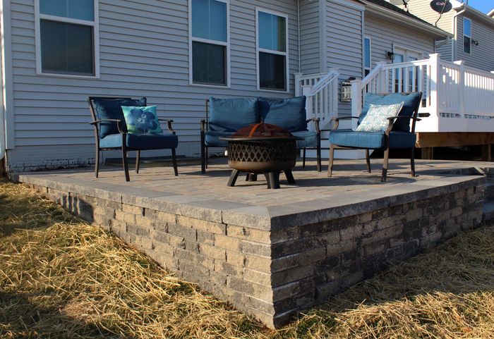 Patio with seating, fire pit, and raised retaining wall in front of a house.