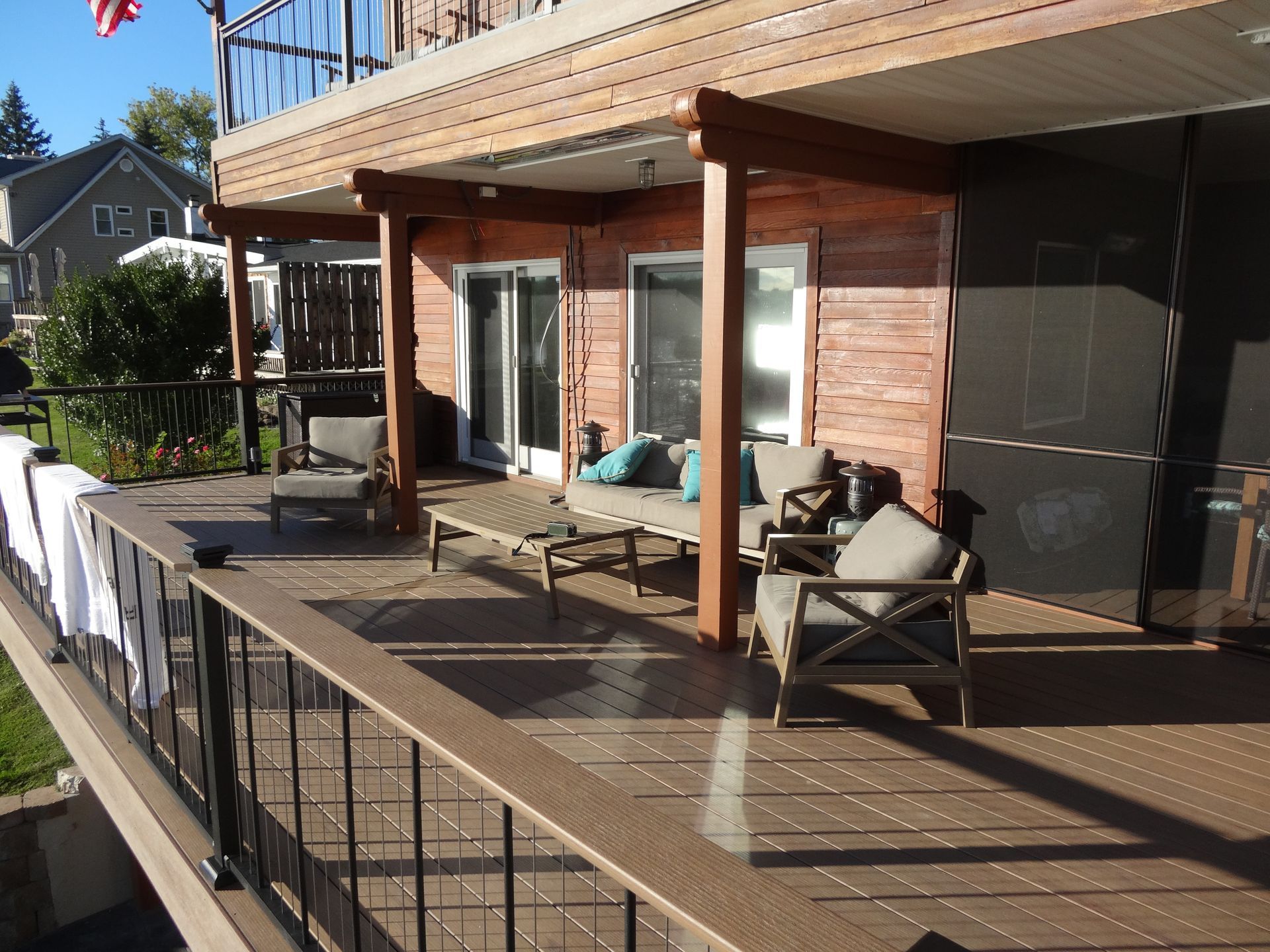 A wooden deck with seating, overlooking a grassy area. Brown and gray furniture, red brick building.
