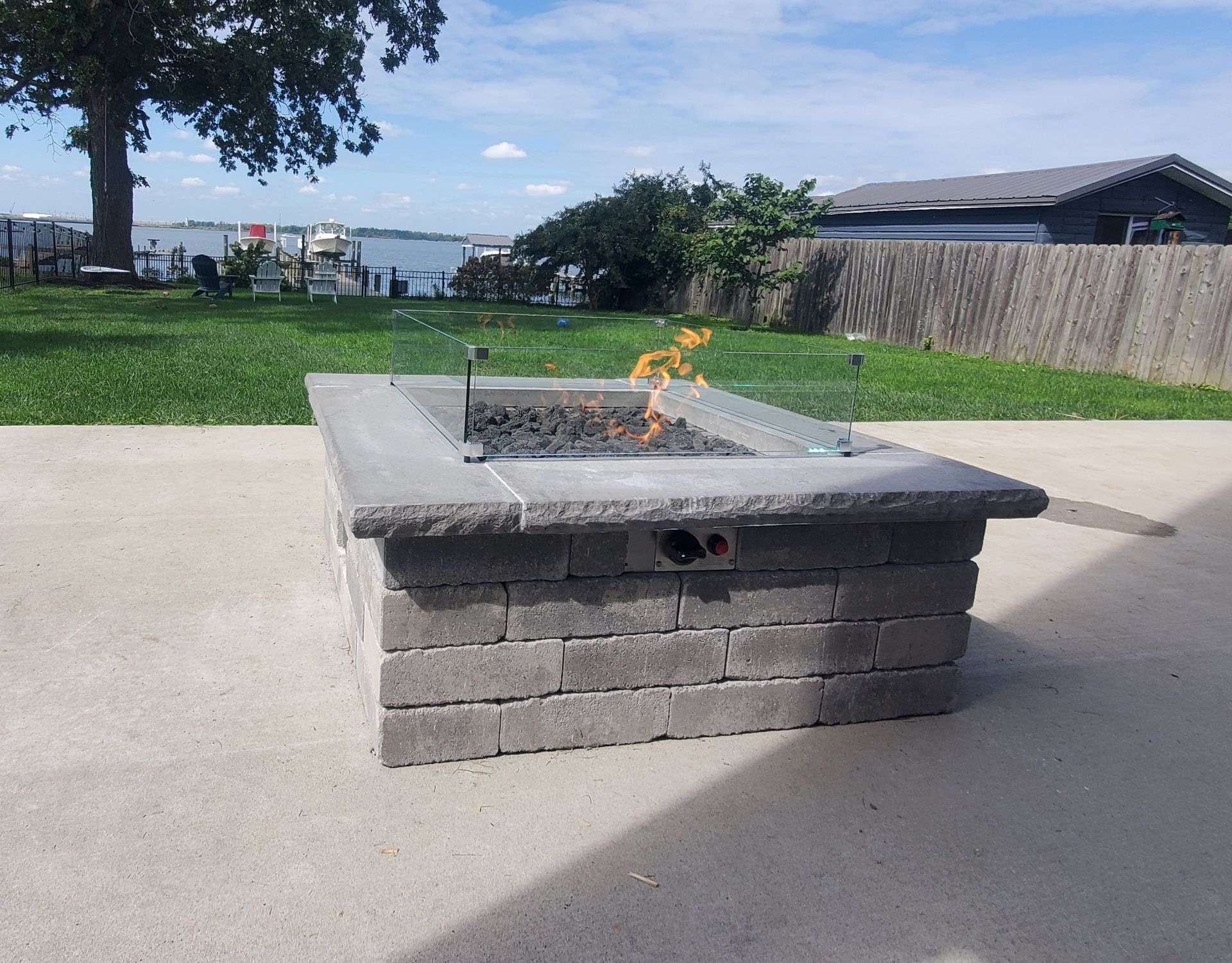 A stone fire pit with a small flame burning on a concrete patio, backyard view.