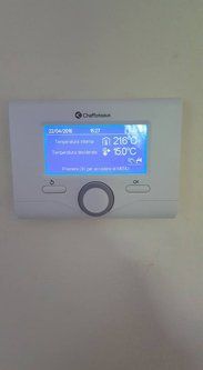 Termostato digitale bianco a parete che visualizza data/ora e temperatura ambiente/impostata.