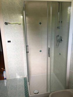 Una cabina doccia con porte in vetro smerigliato in un bagno con piastrelle azzurre.