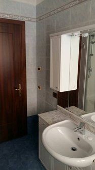 Bagno con lavandino bianco, mobiletto e piastrelle blu. Una porta marrone si trova sulla sinistra.