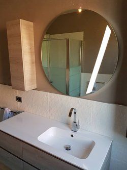 Lavandino del bagno con specchio rotondo che riflette la doccia, mobiletto a muro.