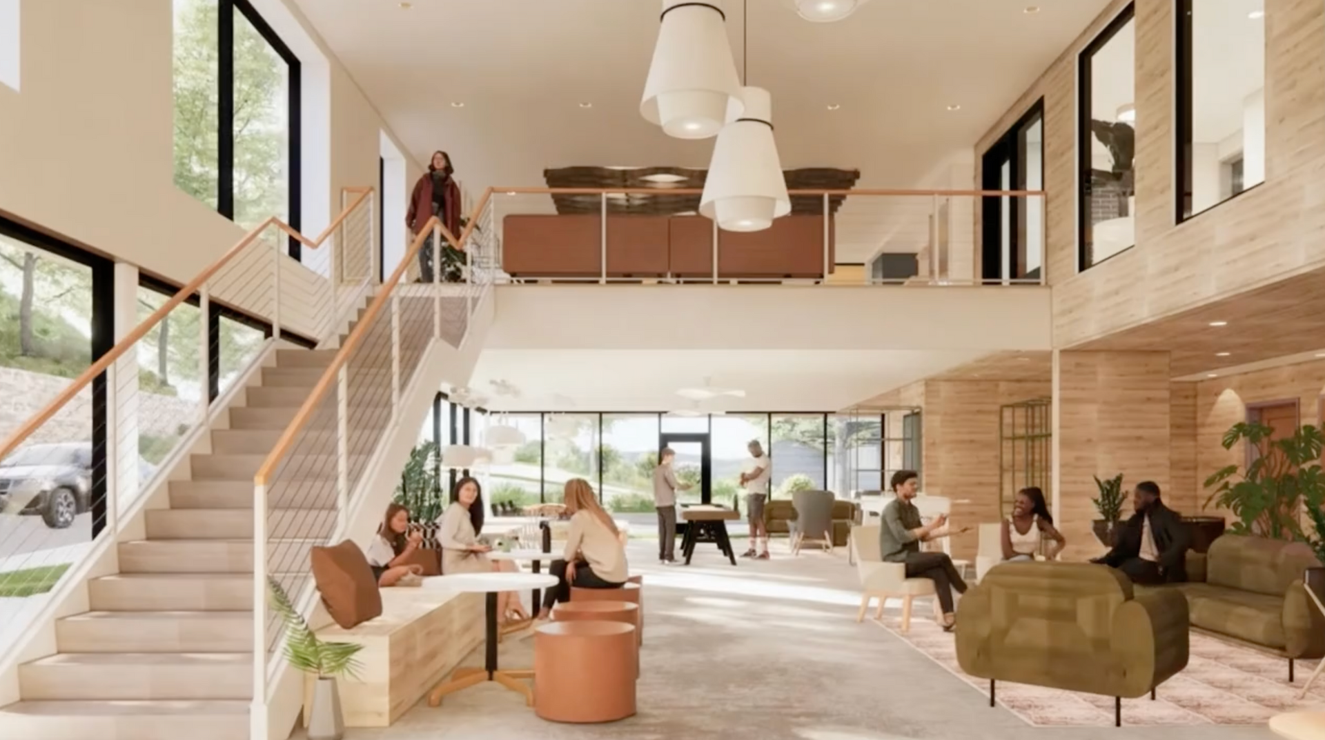 Open-concept interior with staircase and balcony. People sit and stand, interacting in a modern building with large windows.