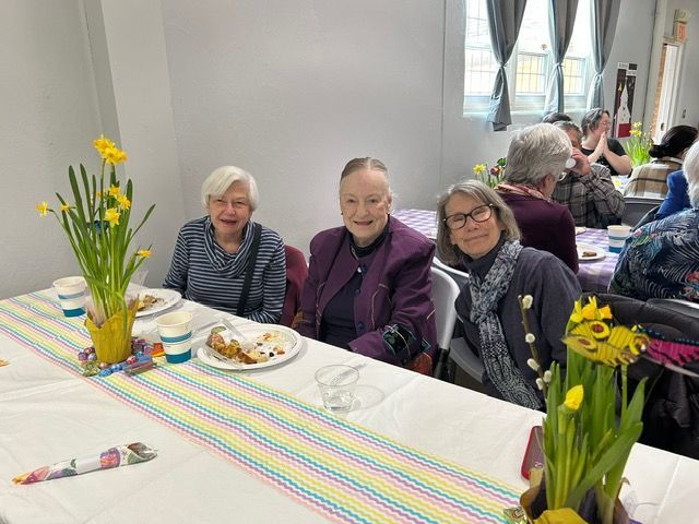 Three people seated at a decorated table with daffodils and food in a bright dining room