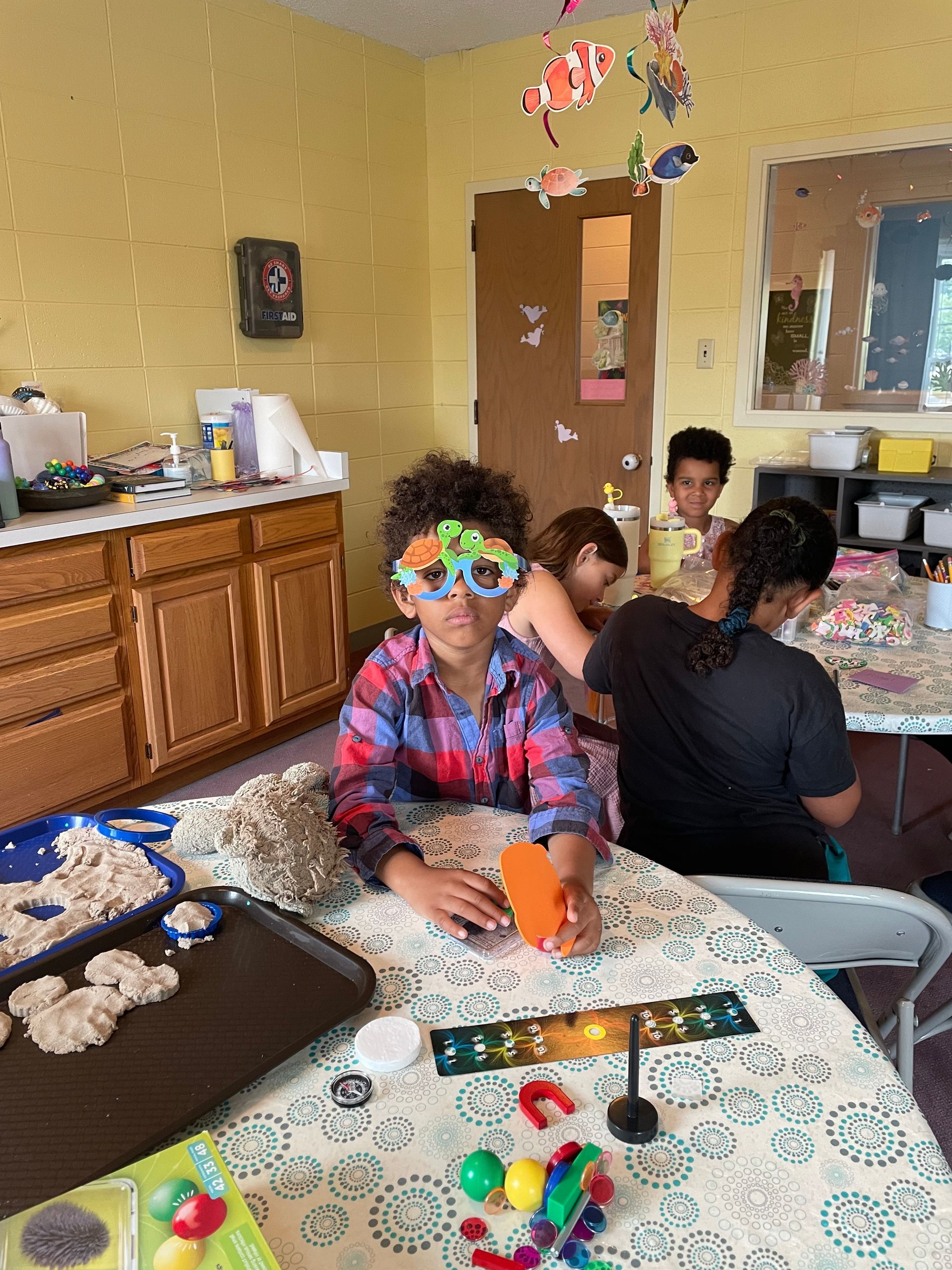 People gathered around a craft table in a kitchen, with colorful paper decorations and supplies scattered nearby.