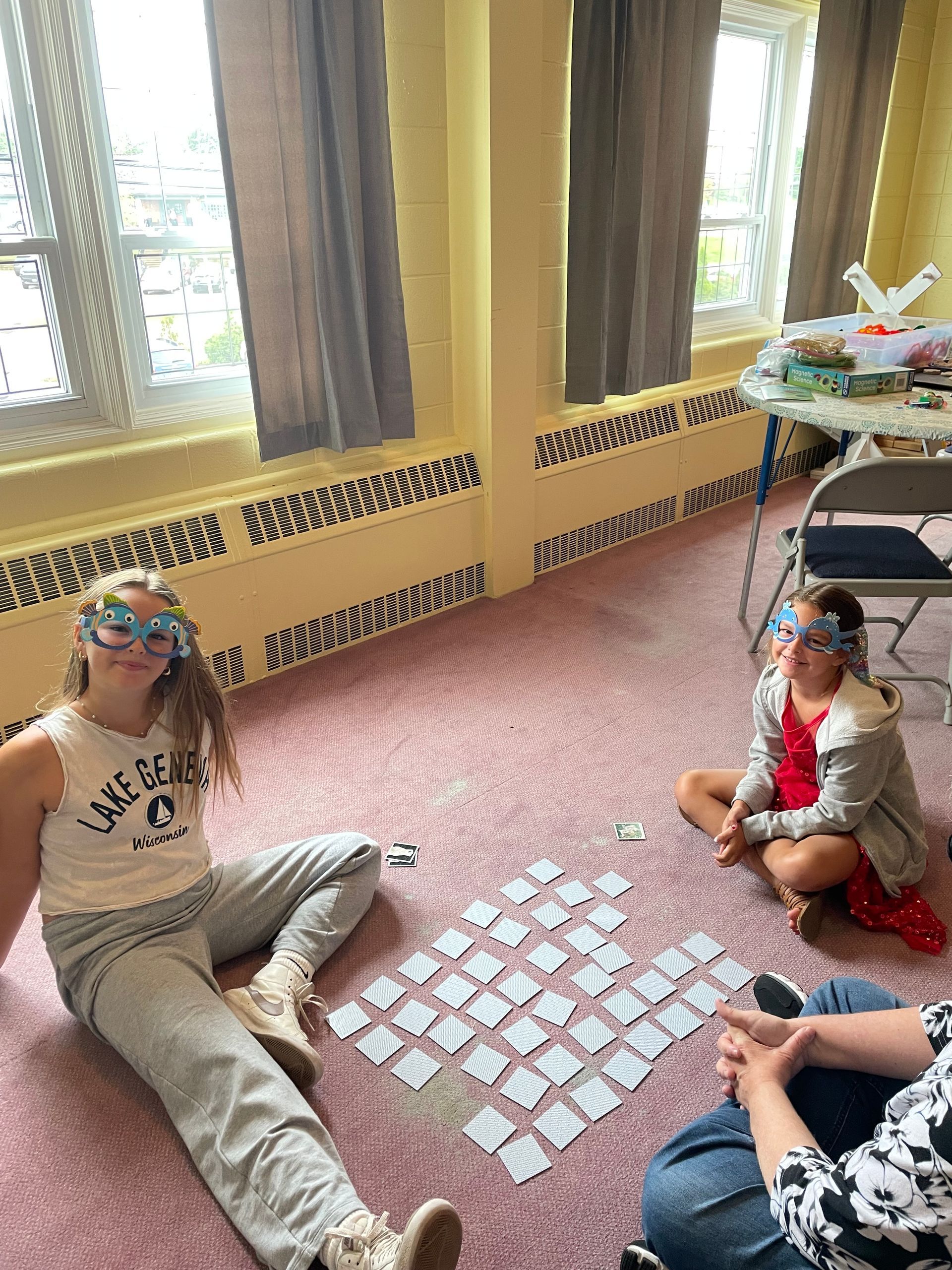 Children sitting on a floor play a matching card game near sunlit windows