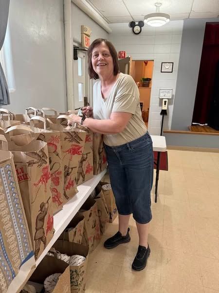 Person smiling while packing paper shopping bags on a table in a small indoor room