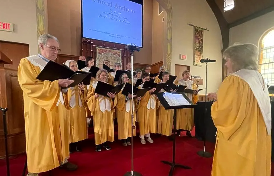 A choir is singing in a church in front of a large screen.