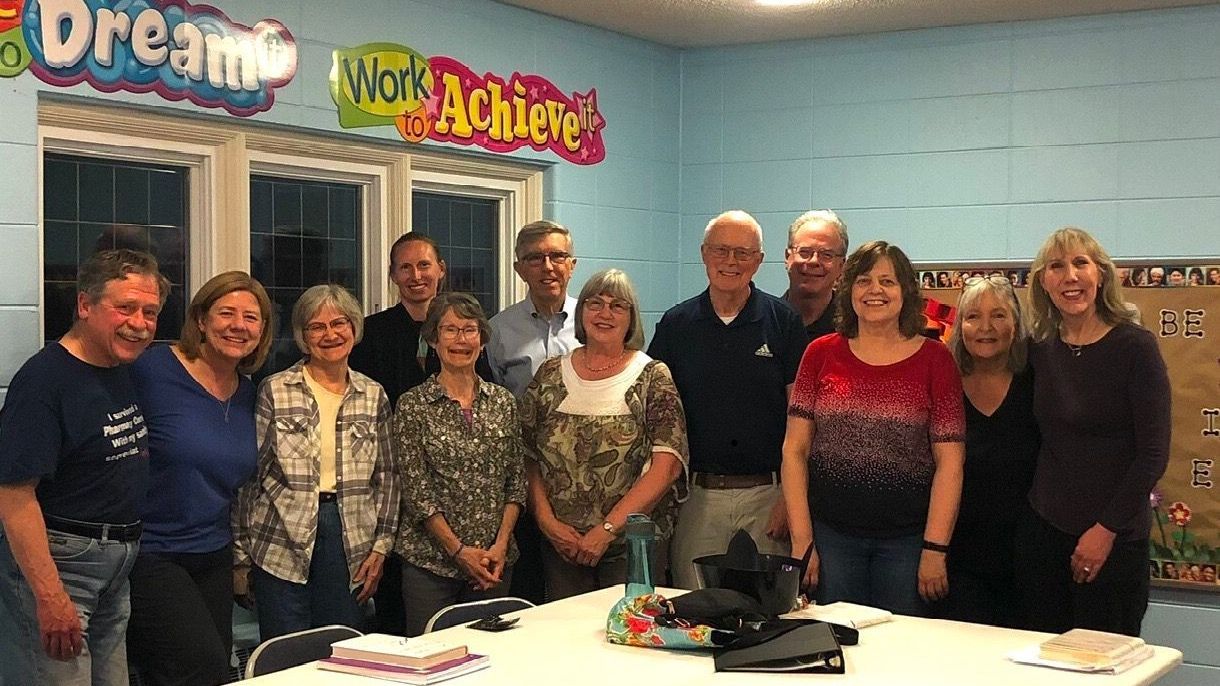 A group of people are posing for a picture in a room with a sign that says dream work achieve