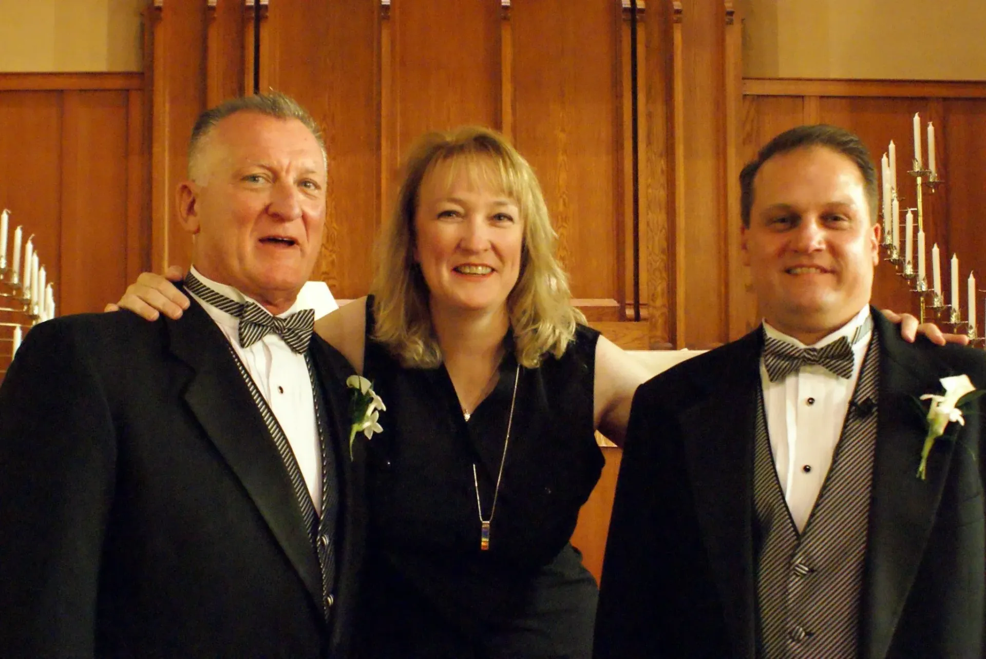 Two men and a woman pose for a picture in front of candles