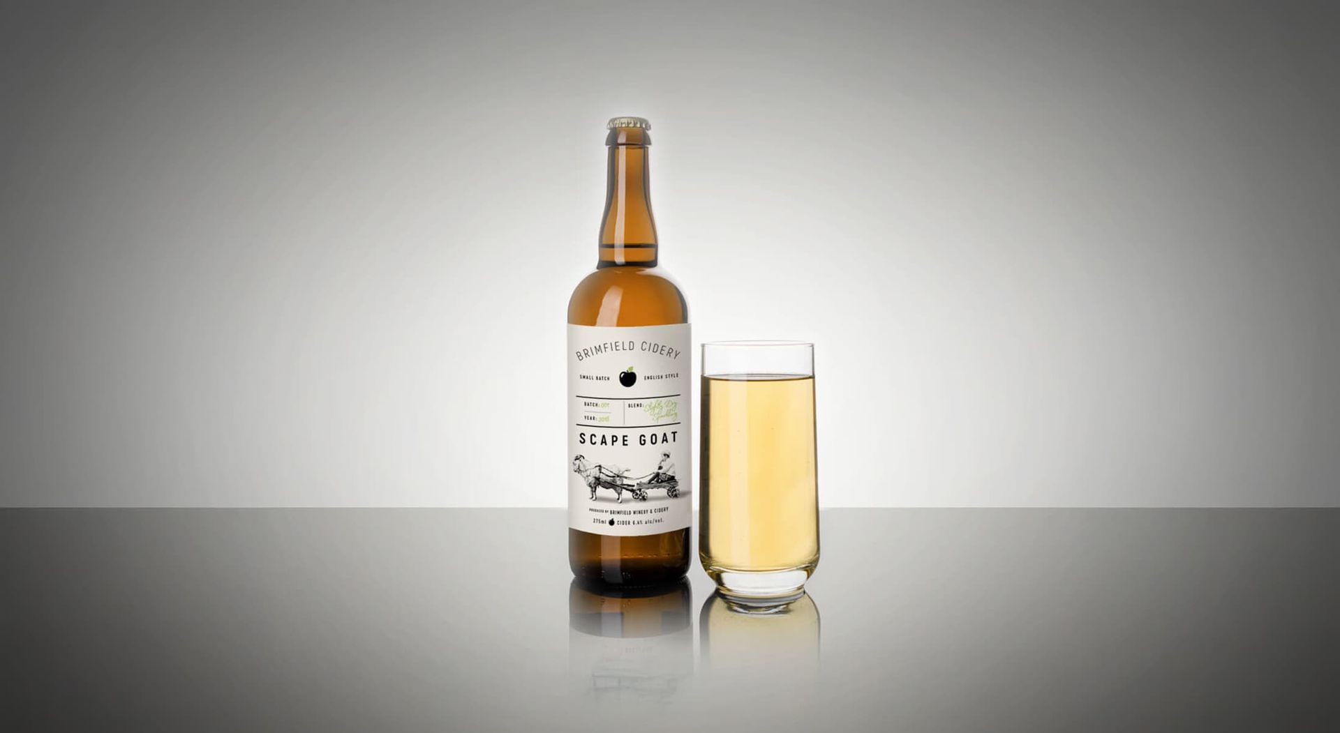 Bottle of light-colored beverage next to a filled glass. Both sit on a reflective surface.