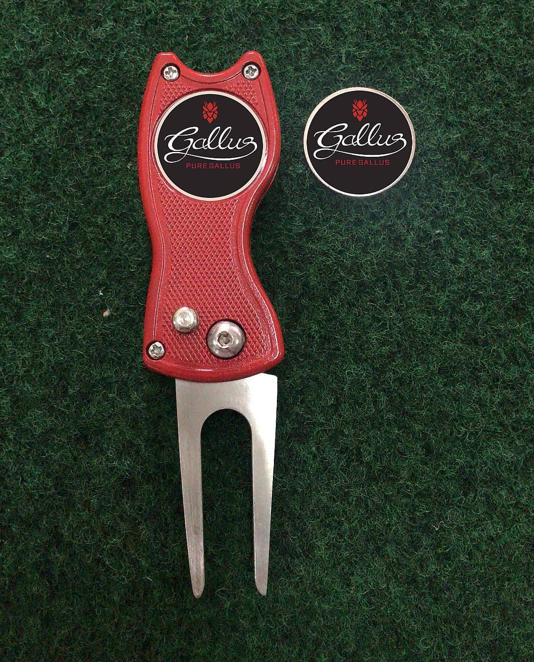 Red golf divot repair tool and ball marker on green turf.
